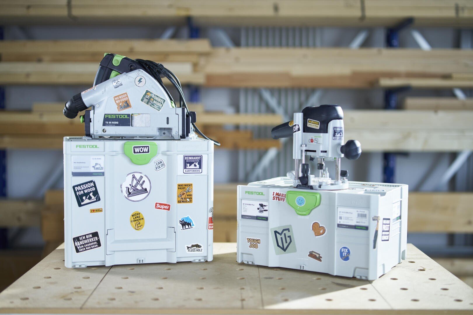 Zwei Elektrowerkzeuge von Festool sitzen auf weißen, mit bunten Aufklebern versehenen Aufbewahrungsboxen auf einer hölzernen Werkbank mit Regalen und Holzbrettern im verschwommenen Hintergrund.